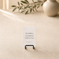 Small dark card stand displaying a Bible verse card on a neutral tabletop